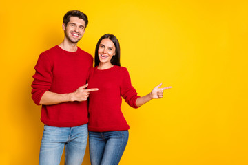 Portrait of charming spouses point at copy space recommend ads wear red pullover sweater denim jeans isolated over yellow background