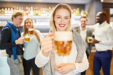 Junge Frau prostet der Kamera zu in einem Pub