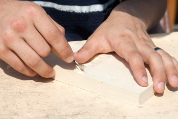A man cuts a pattern with a knife on a wooden surface