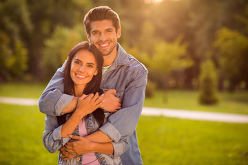 Portrait of lovely spouses with brunet hairstyle cuddling piggyback standing on green lawn wearing...