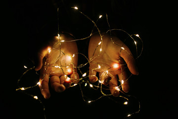 Christmas lights shining warmly closeup. Holding cozy garland in hands.