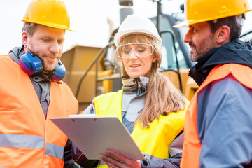 Three workers in a quarry discussing in front of heavy machinery