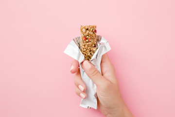 Young woman hand holding cereal bar on pastel pink table. Opened white pack. Closeup. Sweet healthy...