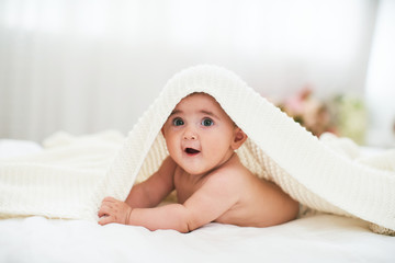 baby under the towel. a cheerful little child looks out from under the blanket and smiles funny. lying on his stomach on their own holds head.