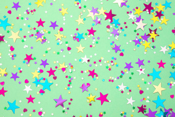 Colorful foil stars confetti sparse on trendy mint colored background. Simple holiday texture. Top view, flat lay