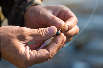 Angler tying a fishing hook to rubber worm lure. Fishing for larva spinning on a lake.