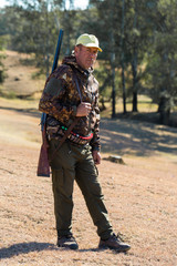 Hunting period, autumn season open. A hunter with a gun in his hands in hunting clothes in the autumn forest in search of a trophy. A man stands with weapons and hunting dogs tracking down the game.	