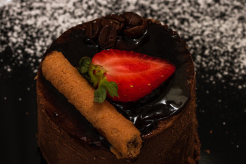 Chocolate mousse with strawberry and chocolate stick on a black dish.