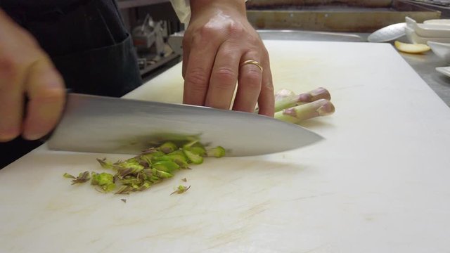 Chef sta tagliando gli asparagi su un tagliere bianco in cucina di un ristorante