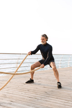 Image of sporty old man doing exercise with battle ropes