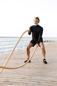 Image of concentrated elderly man doing exercise with battle ropes
