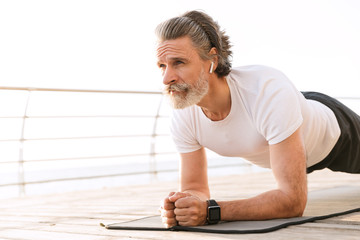 Image of serious mature man using earpod while doing exercise