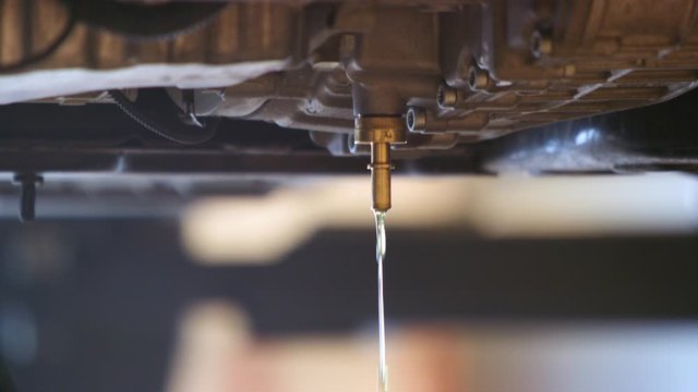Slow pan up of a car being drained of oil
