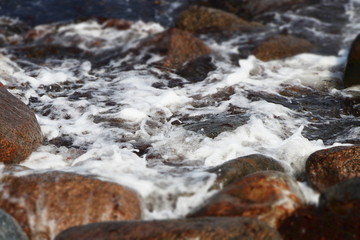 Background with closeup of foamy sea surf on the rocks at the seashore