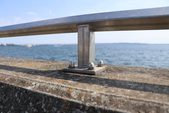Closeup of a metal railing screwed on the concrete of a pier in the harbour