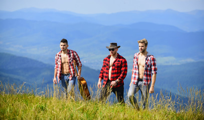 Tourists hiking concept. Enjoying freedom together. Group of young people in checkered shirts walking together on top of mountain. Hiking with friends. Friendly guys with guitar hiking on sunny day