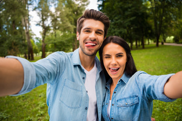 Close up photo of childish spouses with brunet hair making photo showing their tongues winking blinking wearing denim jeans shirt outdoors