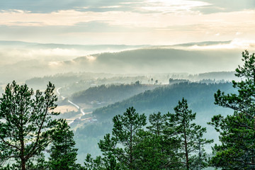 View from the mountain top over foggy Scandinavian mountains with wild pine tree forest, the village, mountain ridges, summer day with heavy dramatic clouds, North Sweden