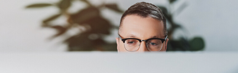 panoramic shot of man in glasses looking away in office