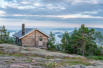 Public tourist rest house in front of view over Scandinavian mountains with pine tree forest, the village and two sea bays, summer day with heavy dramatic clouds, North Sweden