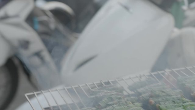A daylight extreme closeup shot of a local vendor preparing a popular Vietnamese meat delicacy wrapped in betel leaves for cooking in a steel charcoal grill..