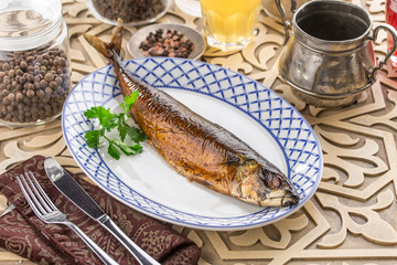 Hot smoked herring fish on plate and glass of lemonade on oriental wooden table