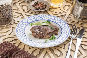 piece of boiled beef on a plate with broth and herbs on oriental wooden table
