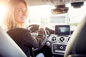 Image of young blonde looking at camera while sitting at wheel of car.