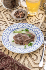 piece of boiled beef on a plate with broth and herbs on oriental wooden table