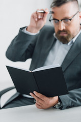 handsome businessman in formal wear and glasses holding pen and notebook