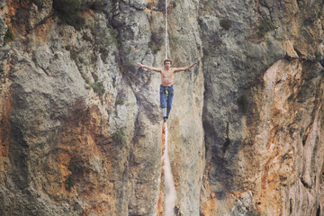 A man is walking along a stretched sling. Highline in the mountains. Man catches balance. Performance of a tightrope walker in nature. Highliner on the background of the mountains.