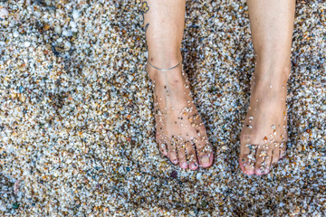 Female legs covered with pebbles on beach