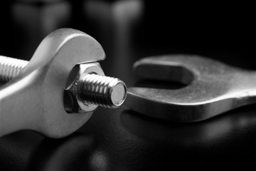 Unscrewing the bolt with a wrench. Wrench and bolt closeup. Wrench tool on a dark background.