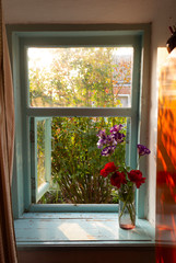 The window in the old residential building is open in the morning in the summer, the rose outside the window and a bouquet of flowers on the windowsill, the morning sun sets in the room.