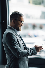 handsome businessman in formal wear and glasses holding smartphone