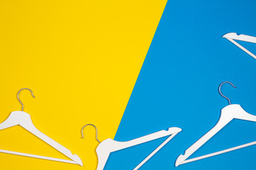 Two white wooden clothes hangers on yellow and light blue background. Shopping, sale, promo, social media, new season concept
