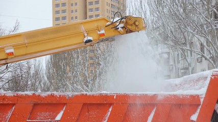 Close-up process of working snow plow. Snow plow loads snow into the truck body. City workers clearing snow from the roads after heavy winter snowfalls.