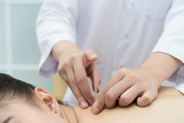 Obraz na płótnie Canvas doctor or Acupuncturist inserting a needle into Asian female neck or back. patient having traditional Chinese treatment using acupuncture to restore an energy flow through specific points on the skin