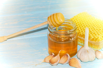 Honey and pieces of garlic on the background of honeycomb. Honey in a glass jar and honeycomb.