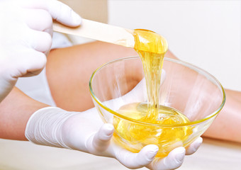 Beautician master holding bowl with hot wax for depilation epilation hair removal procedure and female legs on blurred background