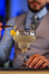 Alcoholic cocktail and a bartender putting garnish on the glass.