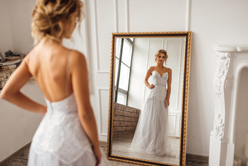 the bride in a beautiful dress looks in the mirror