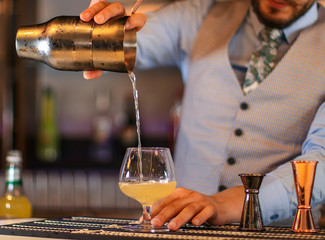 Fototapeta na wymiar Cocktail on a bar in a tall glass and a bartender putting garnish.