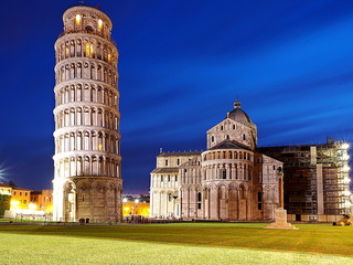 pisa cathedral and pisa tower at night illuminated by street lamps and with a blue sky in the background