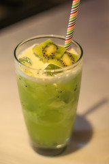 Green fruit cocktail in a tall glass with a straw at a bar.
