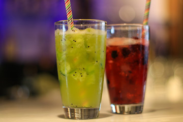 Cocktails red and green at a bar. Non alcoholic fruit mocktails in glasses with straws.