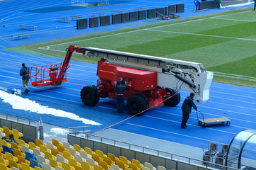 Workers preparing a truck mounted boom lift for repairing sports lighting fixtures of the stadium © Yurii Zushchyk
