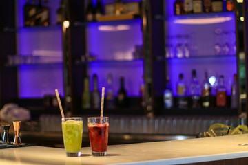 Cocktails red and green at a bar. Non alcoholic fruit mocktails in glasses with straws.