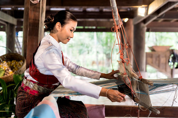 side view of Asian woman weaving silk sari on loom. female works on cotton or silk weaving with traditional hand weaving loom. Asian traditional culture. concept of life, people and Small business