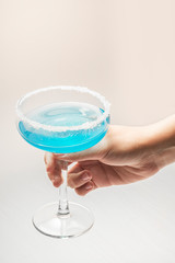 Hand with a glass of cocktail in blue on a light isolated background